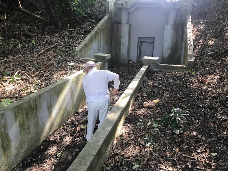 枯れ木や落ち葉が積もっている沖縄のお墓を清掃している様子